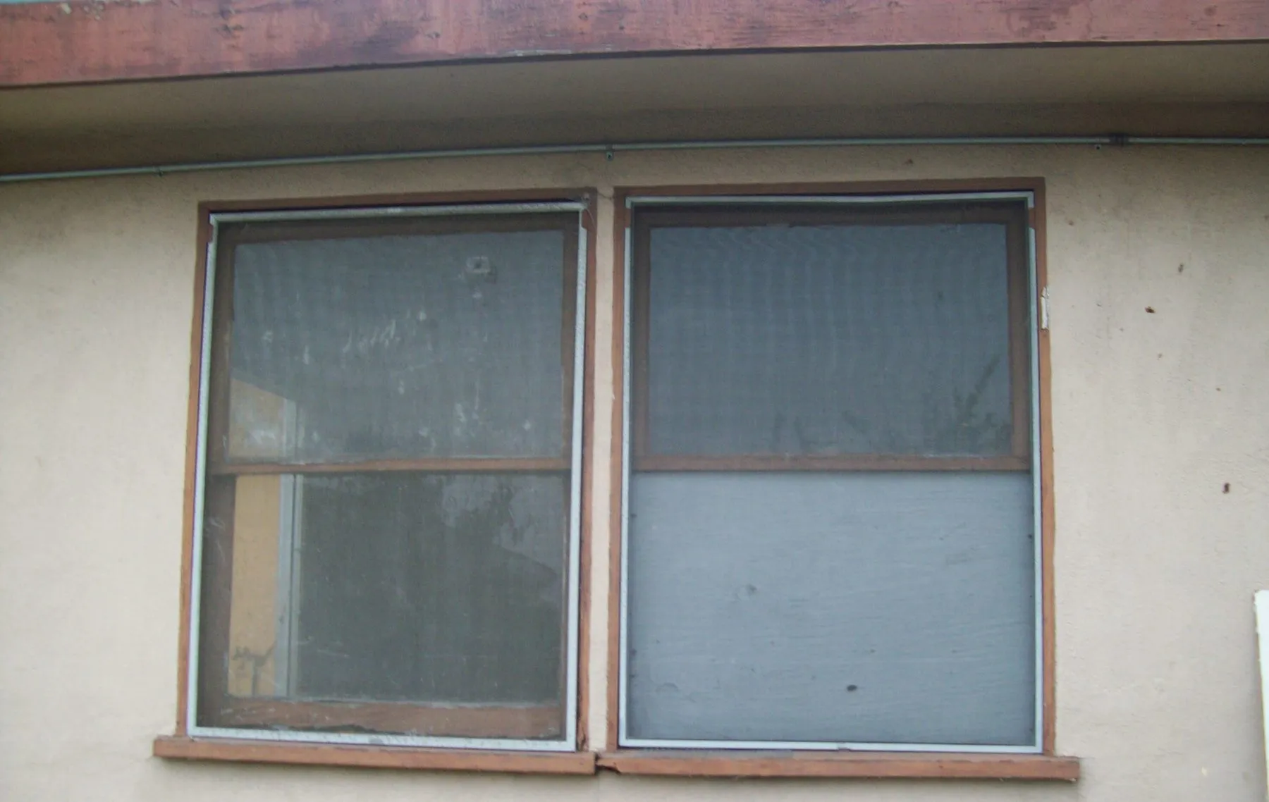 Old aluminum-framed corner windows in beige stucco before replacement